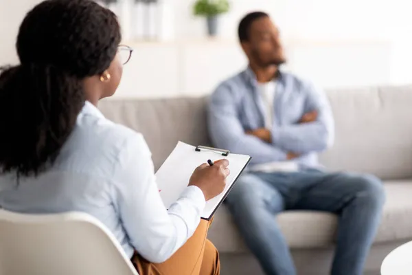 Ung svart man med psykiska problem har session med psykoterapeut på läkarmottagningen, selektivt fokus — Stockfoto