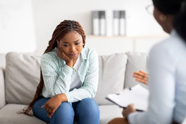 Sad black lady receiving psychological help at mental clinic, communicating with counselor — Stock Photo, Image