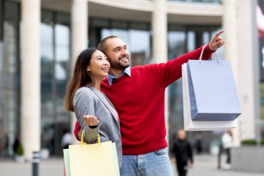 Sokakta ellerinde kese kâğıtlarıyla dolaşan, yeni mağazayı veya reklamı işaret eden, birlikte alışveriş yapan çok yönlü bir çift.