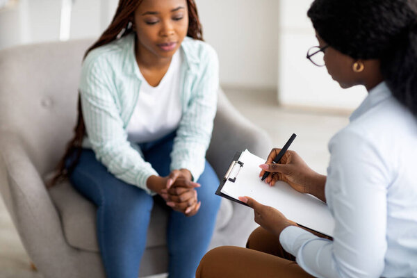 Stressed black female patient consulting psychologist at medical office, selective focus