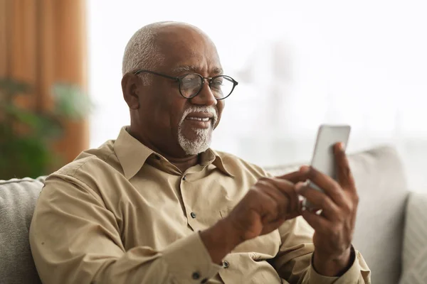 自宅でアプリケーションを使用してスマートフォン上のシニア黒人男性テキスト — ストック写真