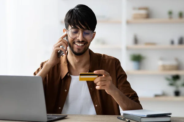 Wesoły człowiek pracujący w biurze, trzymający kartę kredytową, dzwoniący do kogoś — Zdjęcie stockowe
