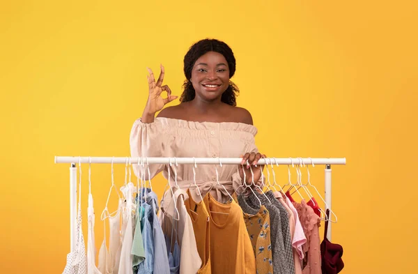 Mooie jonge zwarte vrouw tonen oke gebaar in de buurt van kleding rail vol trendy outfits, aanbevelen kleding winkel — Stockfoto