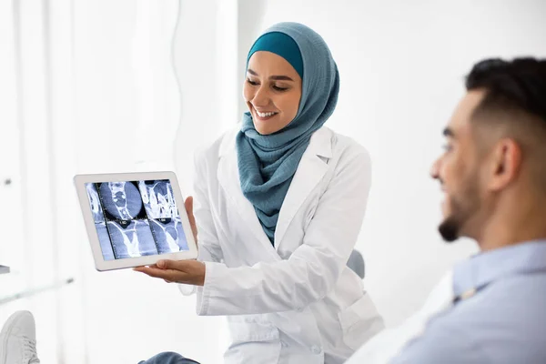 Мусульманський стоматолог тримає цифровий планшет, пояснюючи процес лікування пацієнта — стокове фото