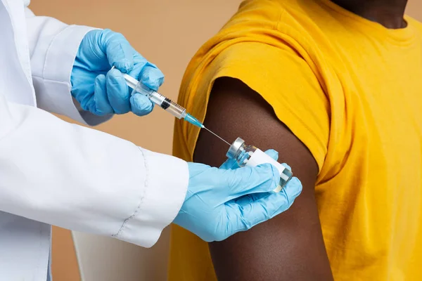 Dokter met injectiespuit neemt vaccin uit injectieflacon, het maken van injectie aan zwarte man — Stockfoto