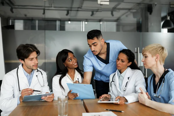 Equipo multiétnico concentrado de médicos sentados en la mesa, conversando —  Fotos de Stock