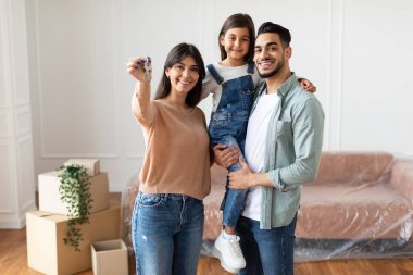 Evlerinin anahtarlarını gösteren üç kişilik mutlu bir aile.