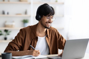 İnternette ders alan genç adam, dizüstü bilgisayarın önünde oturuyor.