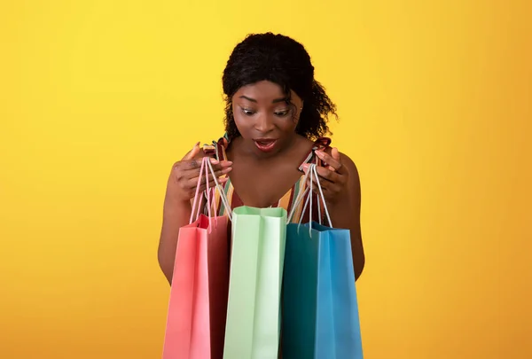 ショッピングバッグの中を見てショックを受けた黒人女性、オレンジスタジオの背景に驚いて — ストック写真