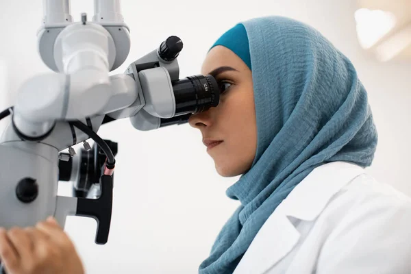 Vrouwelijke tandarts in hidjab werken met moderne tandheelkundige microscoop in de kliniek — Stockfoto