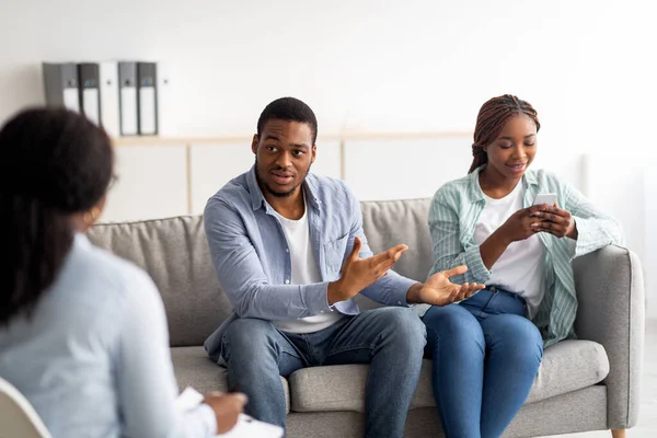 Irritated black guy complaining about his wifes smartphone addiction during psychological consultation at office — Stock Photo, Image