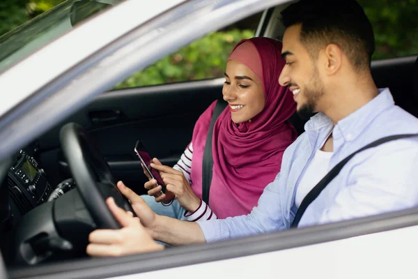 Jonge moslim echtgenoten paardrijden auto en het gebruik van de smartphone samen, door het venster neergeschoten — Stockfoto