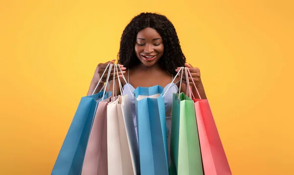 明るいショッピングバッグの中を見て美しい若い黒人女性,幸せな彼女の購入によってオレンジの背景 — ストック写真