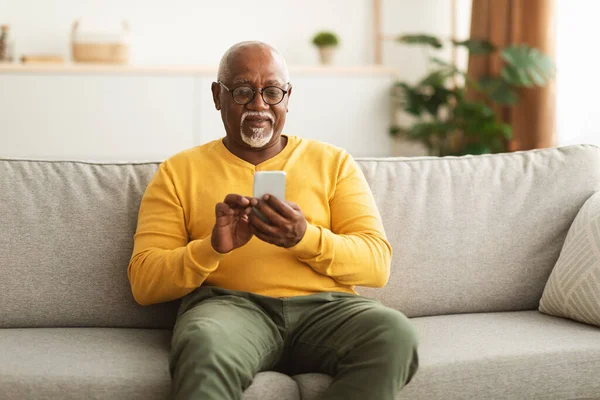 自宅に座っているスマートフォンのテキストメッセージを使用してシニア黒人男性 — ストック写真