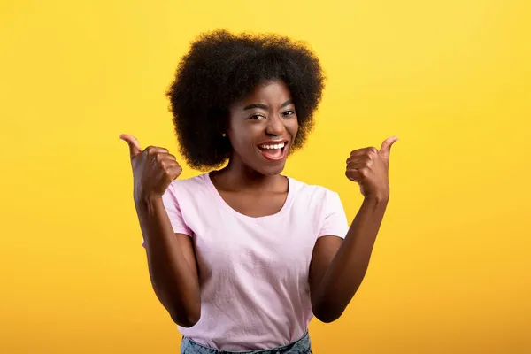 En iyi seçenek. Mutlu Afrikalı Amerikalı kadın iki eliyle baş parmak işareti yapıyor, sarı stüdyo duvarında poz veriyor. — Stok fotoğraf