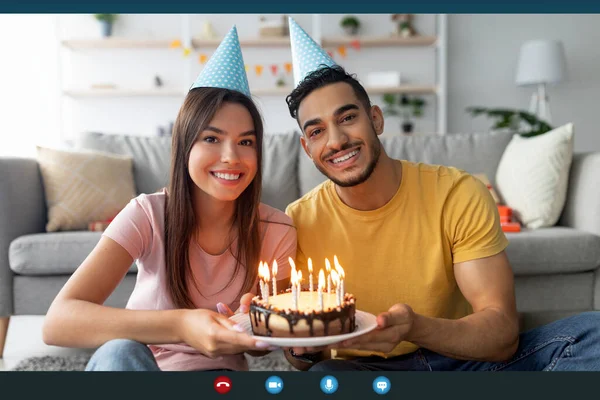 Вид на экран счастливой многорасовой пары, показывающей торт со свечами в веб-камере, празднующей день рождения в Интернете — стоковое фото