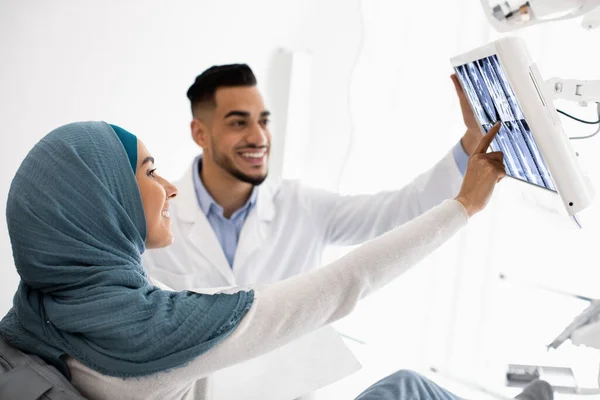 Mujer musulmana mirando los dientes de rayos X mientras recibe tratamiento en la clínica dental —  Fotos de Stock