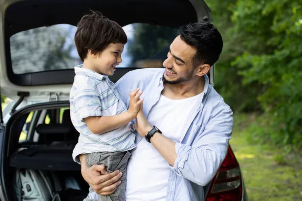 Щасливий арабський чоловік з маленьким сином стоїть біля автомобіля з відкритим слідом — стокове фото