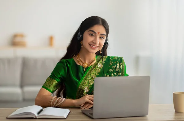Indiase vrouw in sari jurk het dragen van een koptelefoon, het hebben van online vergadering of web conferentie op laptop thuis — Stockfoto
