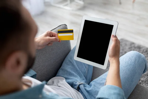 Αγνώριστος νεαρός που κάθεται στον καναπέ, κρατώντας πιστωτική κάρτα, ψωνίζοντας online σε ψηφιακή ταμπλέτα στο σπίτι, mockup — Φωτογραφία Αρχείου