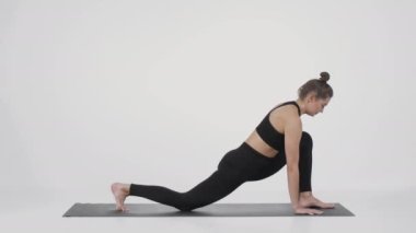 Spor düşkünü, esnek bir kadın spor minderinde yoga yapıyor bacaklarını esnetiyor ve köpek pozisyonunda dikiliyor.