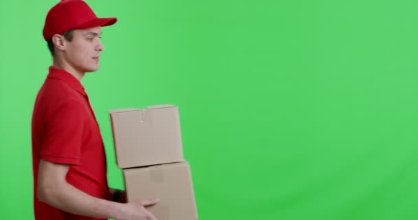 Joven mensajero en uniforme rojo llevando paquetes a la cámara — Vídeos de Stock
