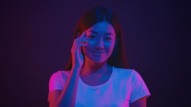 Joven positivo asiático mujer golpeando en el templo, mostrando en su cerebro y sonriendo a la cámara en brillante neón púrpura luces — Vídeos de Stock