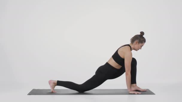 Ung sportig flexibel kvinna tränar yoga på träningsmatta, sträcker på benen och står i nedåtgående hundposition — Stockvideo