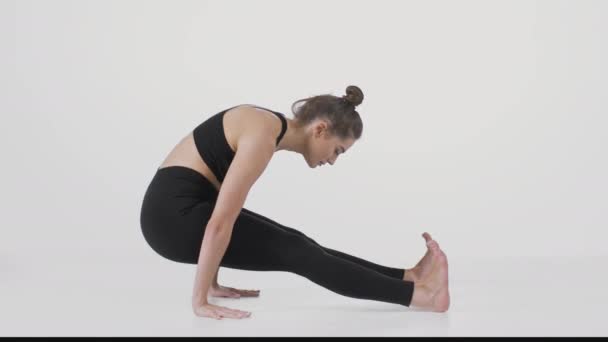 Junge aktive Dame praktiziert Yoga auf weißem Studiohintergrund, schwingt vorwärts und rückwärts auf ihren Händen — Stockvideo