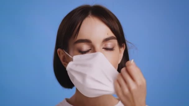 Damen som tar av masken etter Covid-19-rekonvalesens, blå bakgrunn – stockvideo