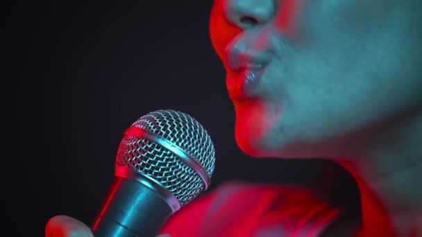 Profesjonalny piosenkarz. Młoda, podniecona, nierozpoznawalna kobieta śpiewająca do mikrofonu, występująca w neonach, widok z boku — Wideo stockowe