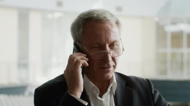 Ώριμος επιχειρηματίας μιλώντας στο κινητό τηλέφωνο κάθεται στο σύγχρονο γραφείο — Αρχείο Βίντεο