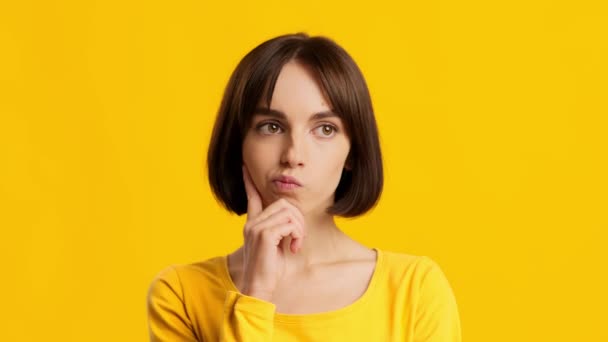 Mujer pensando y señalando dedo hacia arriba tener idea, fondo amarillo — Vídeos de Stock