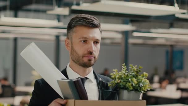 Разочарованный уволенный ходячий человек, держащий картонную коробку, покидающий современный офис — стоковое видео