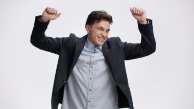 İş başarısı. Takım elbiseli genç işadamı beyaz stüdyo arka planında dans ediyor, galibiyeti ve başarıyı kutluyor.