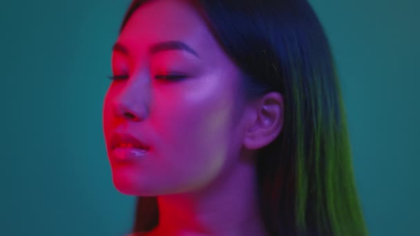 Студийный портрет молодой кореянки тысячелетия, повернувшейся к камере и улыбающейся, позирующей в ярком неоновом свете — стоковое видео