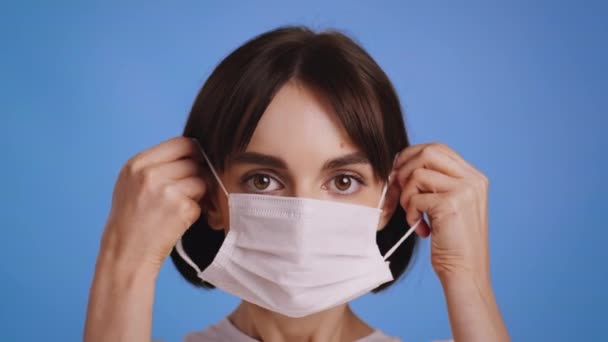 女性は、コロナウイルスの予防のための顔マスクをつける,青の背景 — ストック動画