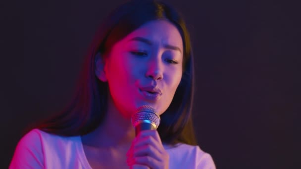 Nightlife entertainment. Young asian woman singing into microphone at karaoke, dancing on stage in bright neon lights — Stock Video