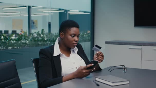 Jovem empresária negra usando cartão de crédito e smartphone no local de trabalho no escritório — Vídeo de Stock