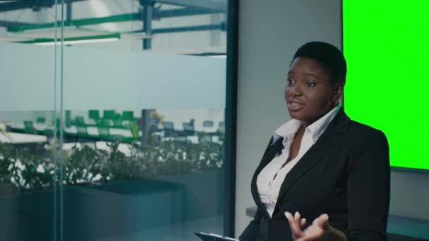 Negro mujer emprendedora haciendo presentación cerca de la pantalla clave de croma verde en la oficina — Vídeos de Stock