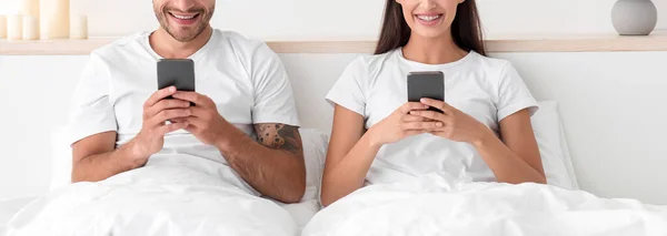 Обрізаний усміхнений кавказький молодий чоловік і жінка друкують на смартфонах, спілкуються онлайн і серфінгують в Інтернеті — стокове фото
