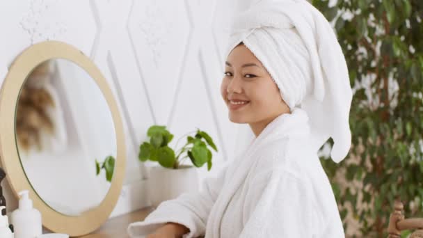 Природные красоты и ухода за кожей. Молодая счастливая азиатка прикасается к своей идеальной коже, сидя в ванной комнате — стоковое видео