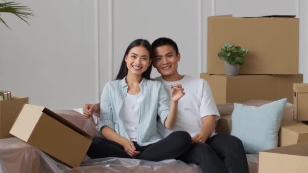 Pareja japonesa mostrando la llave sentada entre cajas en un nuevo hogar — Vídeos de Stock