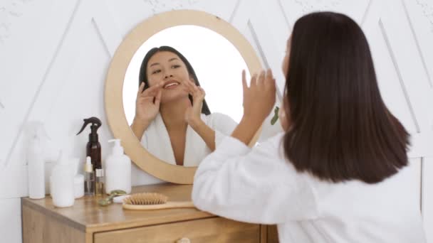 Junge attraktive koreanische Frau schaut in den Spiegel, lächelt zu sich selbst, genießt ihre Jugend und Schönheit, sitzt im Badezimmer — Stockvideo