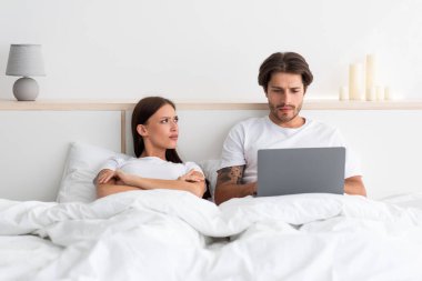 Canı sıkkın, güvenilmez, kıskanç, bin yıllık Avrupalı kadın kocasına bakıyor, adam dizüstü bilgisayarında çalışıyor.