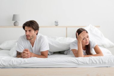 Kızgın, genç, beyaz bir çift yatakta yatarken yatak odasında partnerini görmezden geliyor.