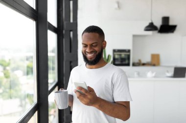 Siyah adam akıllı telefonuyla kahve içerken mesaj atıyor.
