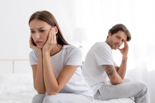 Dühös sértett Millenniumi európai feleség ül az ágyon figyelmen kívül hagyva a szomorú férj fehér hálószobában — Stock Fotó