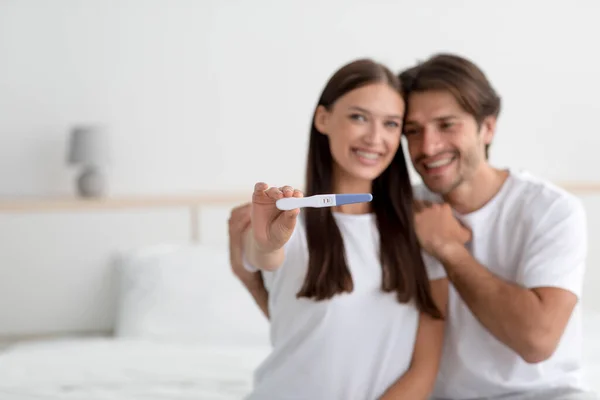 Glücklich zufrieden millennial europäischen Mann und Frau freuen, zeigen Schwangerschaftstest auf Bett im Schlafzimmer — Stockfoto