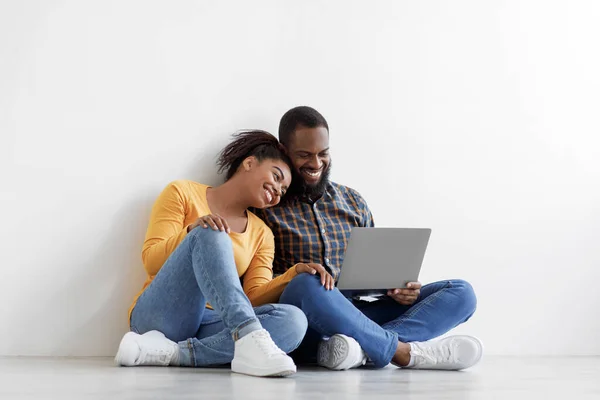 Jovem feliz marido e mulher negra sentados no chão em quarto vazio, planejando novo interior no fundo da parede branca — Fotografia de Stock